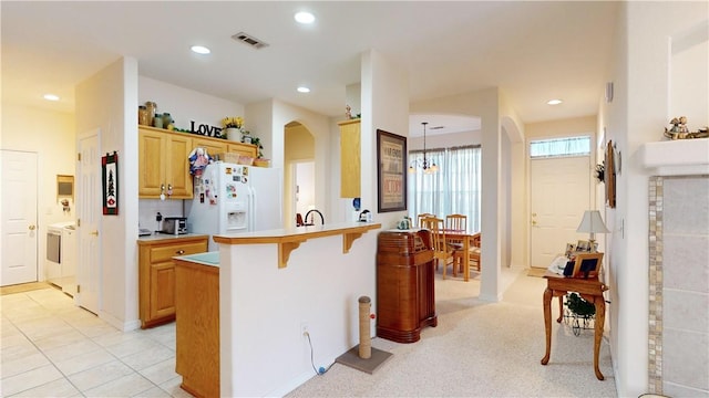 kitchen with a breakfast bar, light brown cabinets, white refrigerator with ice dispenser, an inviting chandelier, and hanging light fixtures