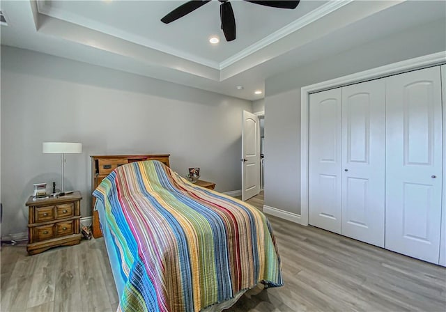 bedroom featuring ceiling fan, a raised ceiling, light hardwood / wood-style flooring, crown molding, and a closet