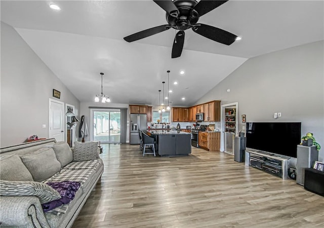 living room with light wood-type flooring, ceiling fan with notable chandelier, and high vaulted ceiling