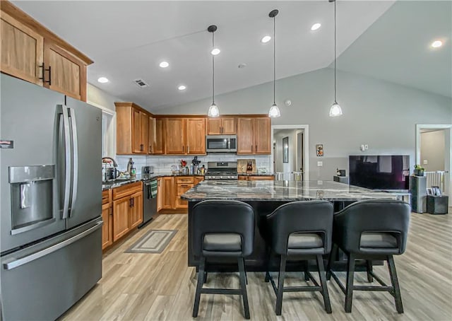 kitchen with pendant lighting, a breakfast bar, dark stone counters, decorative backsplash, and appliances with stainless steel finishes