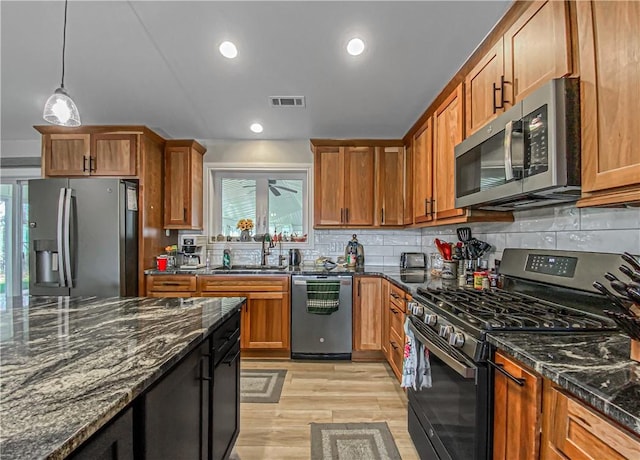 kitchen with pendant lighting, sink, light hardwood / wood-style flooring, dark stone countertops, and appliances with stainless steel finishes