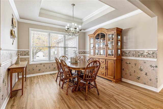 dining area featuring a notable chandelier, a raised ceiling, ornamental molding, and light hardwood / wood-style flooring