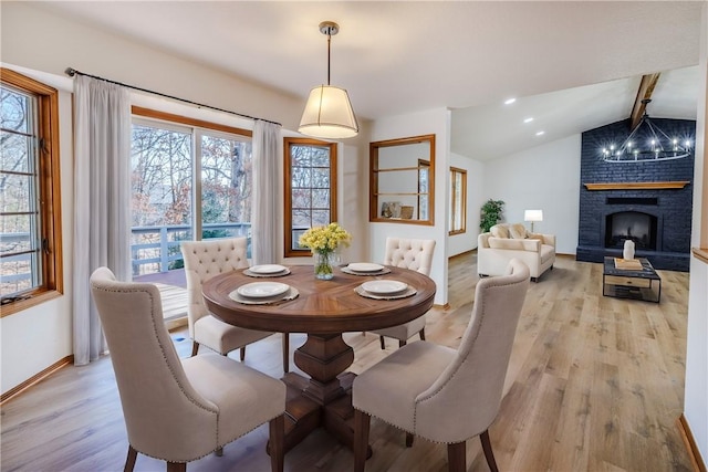 dining space with a chandelier, a fireplace, lofted ceiling with beams, and light hardwood / wood-style floors