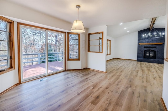 entryway featuring a fireplace, lofted ceiling with beams, light hardwood / wood-style floors, and an inviting chandelier