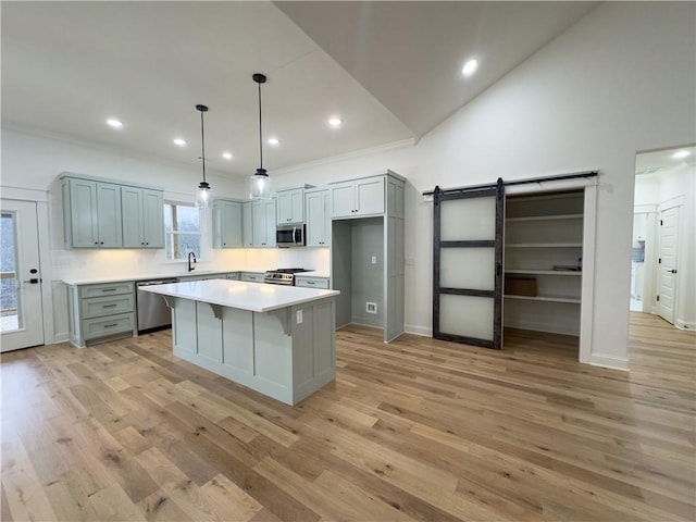 kitchen featuring appliances with stainless steel finishes, a kitchen island, light hardwood / wood-style floors, high vaulted ceiling, and a barn door