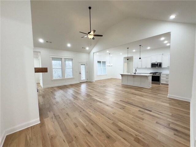 unfurnished living room featuring sink, light hardwood / wood-style floors, ceiling fan with notable chandelier, and high vaulted ceiling