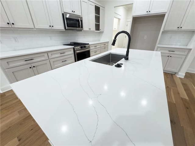 kitchen with light stone counters, appliances with stainless steel finishes, wood finished floors, a sink, and backsplash