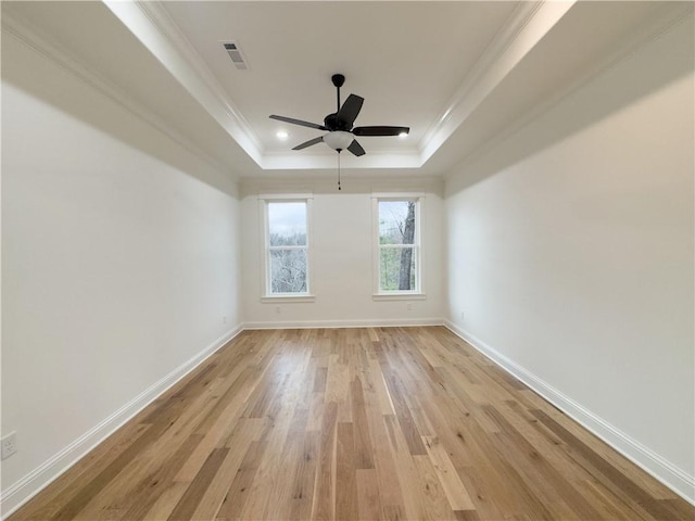 empty room with light wood-type flooring, baseboards, a tray ceiling, and ornamental molding