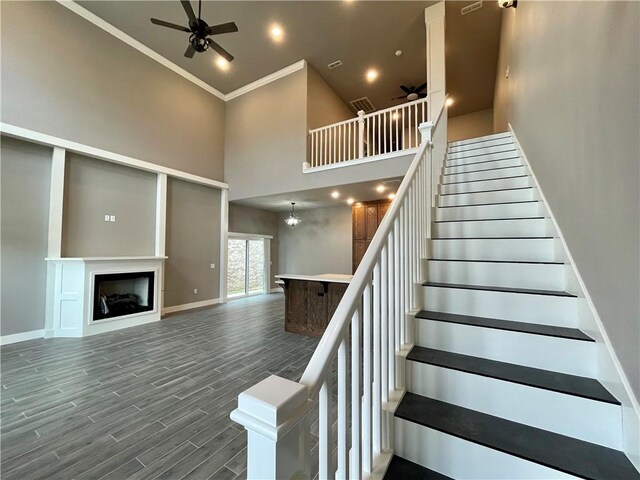 stairway featuring hardwood / wood-style floors, ceiling fan with notable chandelier, a towering ceiling, and crown molding