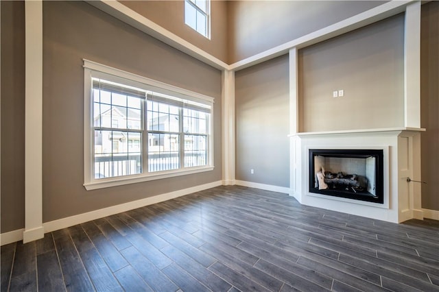 unfurnished living room with a wealth of natural light, dark wood-type flooring, and a high ceiling