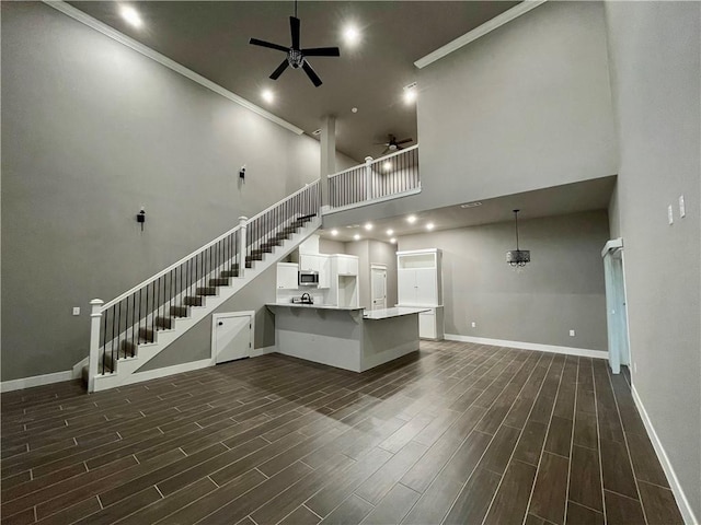 unfurnished living room featuring a towering ceiling, ceiling fan, and crown molding