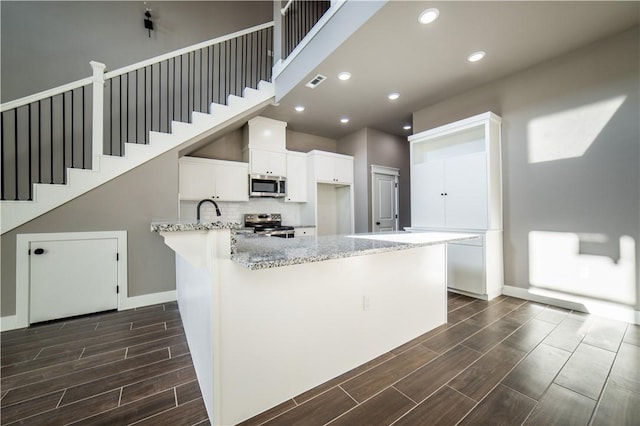 kitchen featuring kitchen peninsula, appliances with stainless steel finishes, light stone countertops, sink, and white cabinets