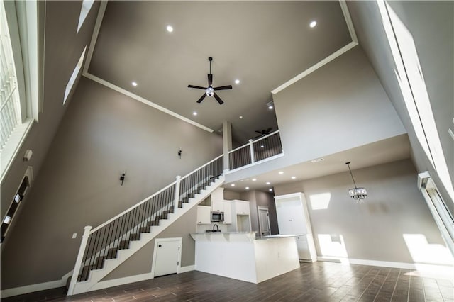 unfurnished living room with ceiling fan with notable chandelier, a high ceiling, and ornamental molding