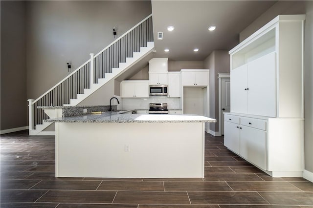 kitchen with sink, kitchen peninsula, light stone countertops, appliances with stainless steel finishes, and white cabinetry