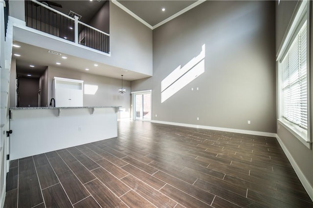 unfurnished living room with a high ceiling, an inviting chandelier, crown molding, and sink