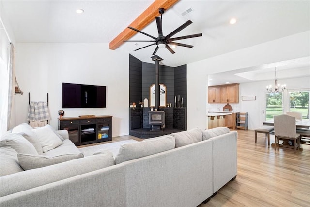 living room featuring ceiling fan with notable chandelier, lofted ceiling with beams, light hardwood / wood-style flooring, and a wood stove