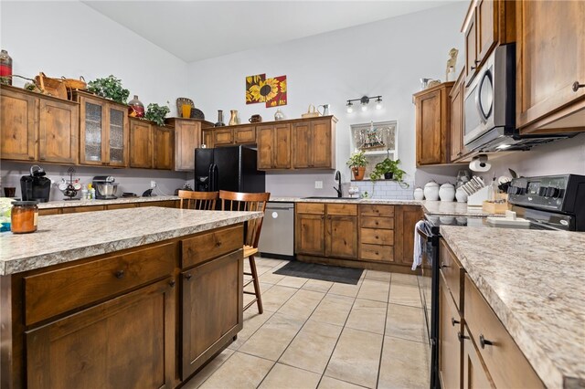 kitchen with black appliances, a kitchen bar, light tile patterned floors, and sink