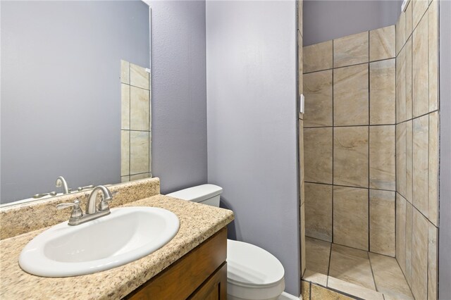 bathroom with tiled shower, vanity, and toilet