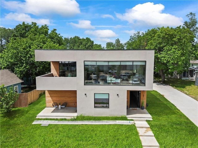 rear view of property with a balcony, stucco siding, fence, and a yard