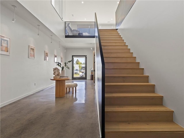 stairs with a towering ceiling, finished concrete flooring, and baseboards