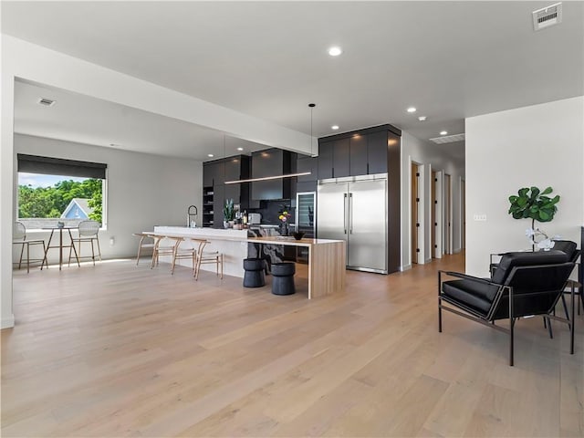 kitchen with pendant lighting, sink, built in refrigerator, tasteful backsplash, and light wood-type flooring