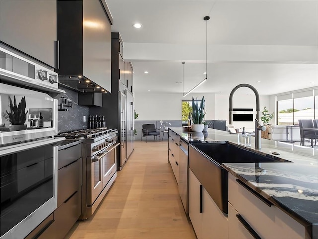 kitchen featuring dark stone countertops, pendant lighting, stainless steel appliances, light hardwood / wood-style floors, and wall chimney range hood