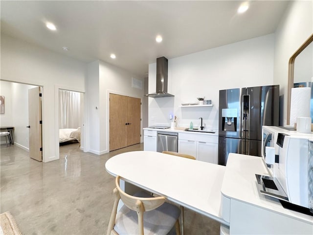 kitchen with recessed lighting, a sink, white cabinets, wall chimney range hood, and appliances with stainless steel finishes