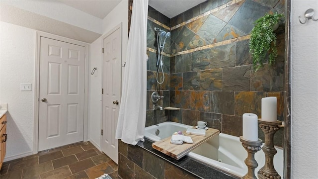 bathroom with stone finish floor, baseboards, tiled shower / bath, and vanity