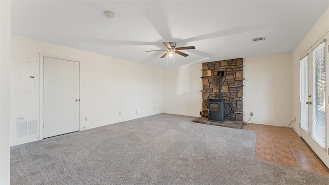 unfurnished living room with carpet floors, visible vents, a ceiling fan, electric panel, and a wood stove