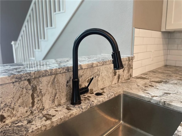 interior details with decorative backsplash, white cabinetry, light stone countertops, and sink