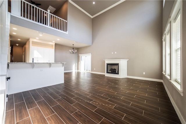 unfurnished living room featuring a high ceiling, ceiling fan with notable chandelier, and crown molding