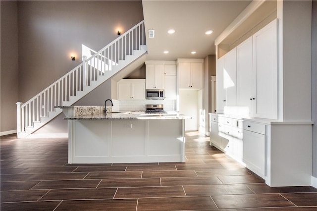 kitchen with backsplash, light stone counters, stainless steel appliances, sink, and white cabinetry