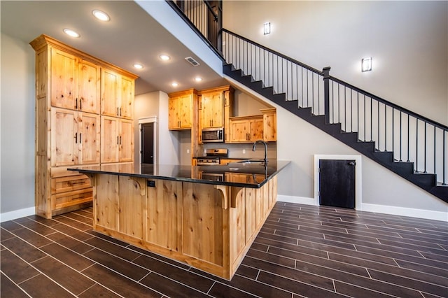 kitchen with kitchen peninsula, a kitchen breakfast bar, stainless steel appliances, sink, and light brown cabinets