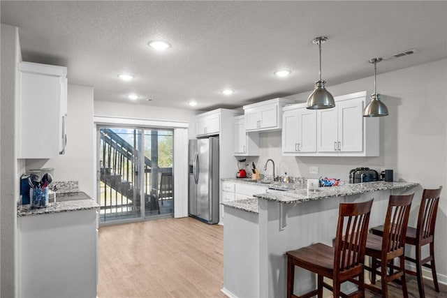 kitchen with a kitchen breakfast bar, light wood-type flooring, pendant lighting, white cabinets, and stainless steel fridge with ice dispenser