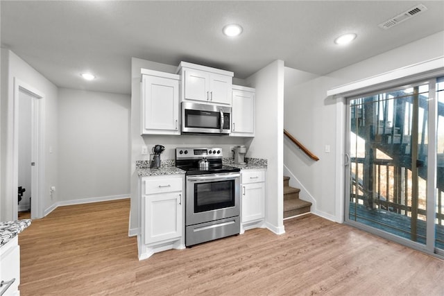 kitchen with light stone countertops, white cabinets, stainless steel appliances, and light wood-type flooring