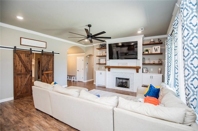 living room featuring ceiling fan, a barn door, crown molding, a fireplace, and hardwood / wood-style flooring