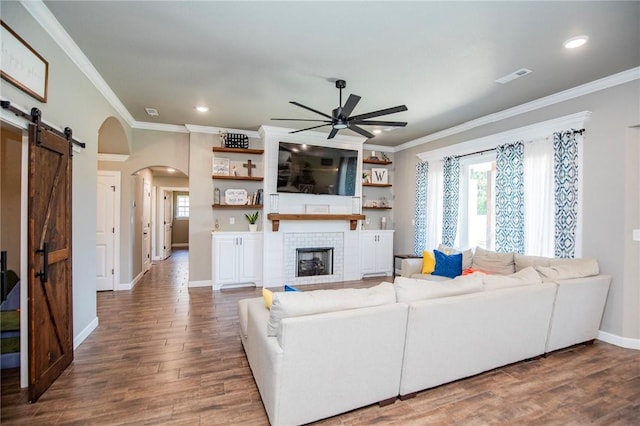 living room with a large fireplace, dark hardwood / wood-style floors, ceiling fan, and crown molding