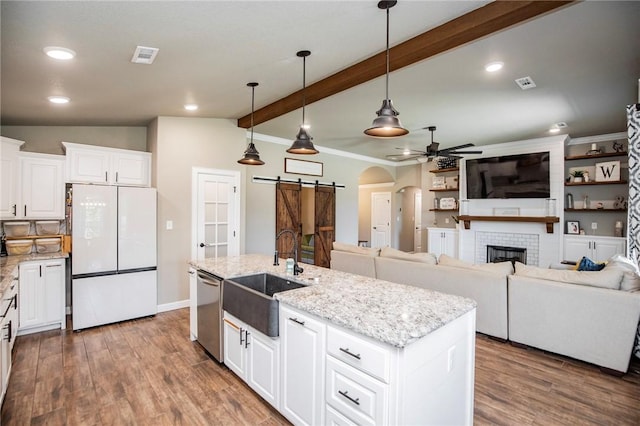 kitchen featuring white refrigerator, decorative light fixtures, a barn door, a center island with sink, and white cabinets