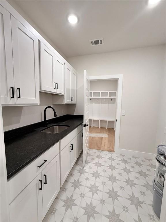 kitchen featuring light floors, visible vents, a sink, white cabinetry, and dark countertops