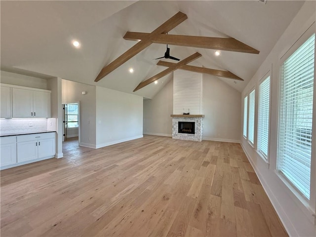 unfurnished living room with baseboards, a stone fireplace, light wood finished floors, and beam ceiling