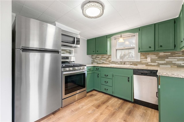 kitchen featuring stainless steel appliances, green cabinetry, sink, light hardwood / wood-style flooring, and backsplash