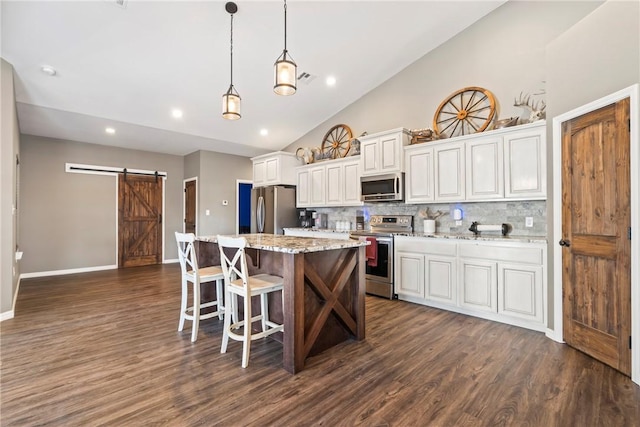 kitchen featuring a barn door, decorative backsplash, light stone counters, and appliances with stainless steel finishes