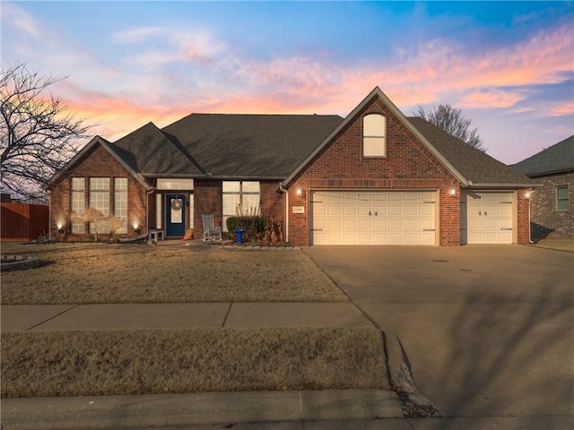 view of front of home featuring a garage, a shingled roof, concrete driveway, and brick siding