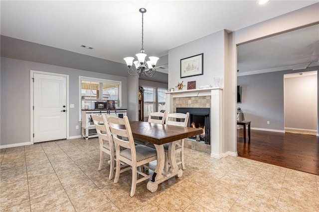 tiled dining space featuring crown molding, a fireplace, and an inviting chandelier