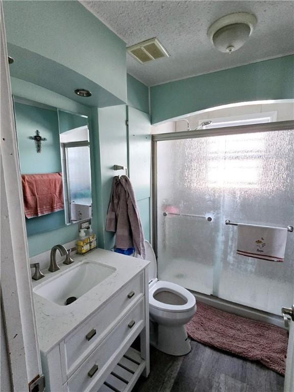 bathroom featuring walk in shower, vanity, a textured ceiling, hardwood / wood-style floors, and toilet