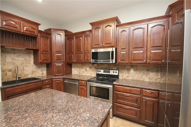 kitchen with appliances with stainless steel finishes, tasteful backsplash, sink, dark stone countertops, and light tile patterned flooring