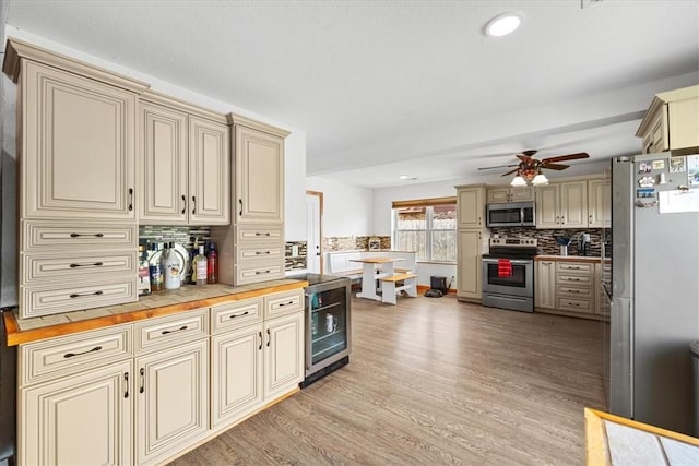 kitchen with stainless steel appliances, wood counters, wine cooler, cream cabinetry, and decorative backsplash