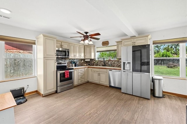 kitchen featuring a healthy amount of sunlight, cream cabinets, appliances with stainless steel finishes, beamed ceiling, and light hardwood / wood-style floors