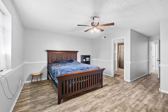 bedroom with a textured ceiling, connected bathroom, hardwood / wood-style flooring, and ceiling fan