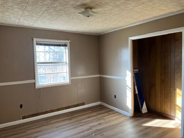 unfurnished room featuring wood walls, wood-type flooring, and ornamental molding